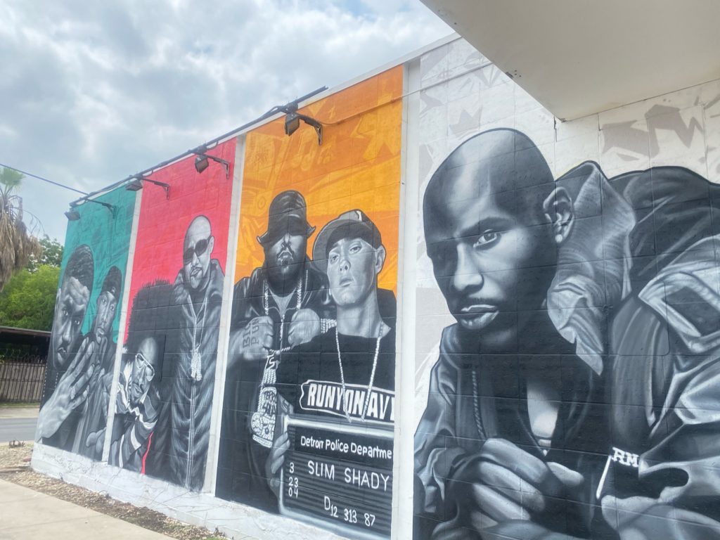 Art mural of rappers, Outkast in teal background, Fat Joe in Pink background, Big Pun and Eminem in Orange-yellow background, and DMZ in white background